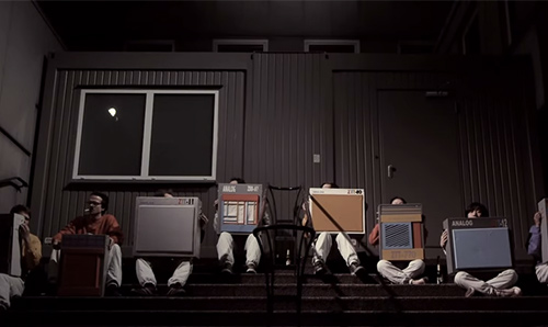 Film still from 'Krach Kisten Orchester Leca Platte' featuring musicians sitting on steps holding speakers.