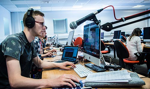 Male student in front of a computer and microphone in the ground floor cluster